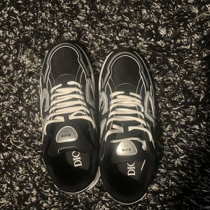 Dior B30 svarta och silver sneakers. Pris går att diskuteras - Säljer ett par Dior B30 sneakers i svart med silvriga detaljer och vit sula. Skorna har tydlig Dior-logga på sidan och tungan, samt vita snören. Ovandelen är i mesh och syntet med coola kontraster och sportig vibe. Perfekta för dig som vill sticka ut med lyxig streetstyle.