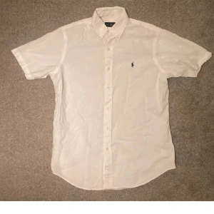 Vit kortärmad skjorta Ralph Lauren - Säljer denna vita kortärmade skjortan från Ralph Lauren. Den är i tunt material och perfekt för sommaren. Kom gärna med prisförslag då priset inte är hugget i sten!