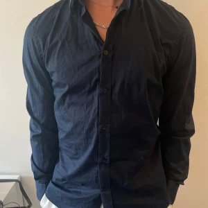 Mörkblå skjorta från Filippa K - Snygg mörkblå skjorta från Filippa K i klassisk modell med knappar hela vägen och lång ärm. Skjortan är i bomull och har en stilren, tidlös look som passar perfekt till jeans eller chinos. Enkel att matcha och riktigt clean i stilen.