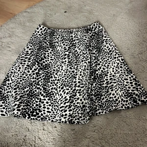 Svartvit leopardmönstrad kortkjol - Snygg svartvit kortkjol med leopardmönster och lätt utställd form. Kjolen har resår i midjan för en bekväm passform och är perfekt för dig som vill sticka ut med ett coolt mönster. Superenkel att matcha med både sneakers och boots.
