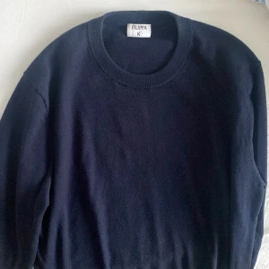 Mörkblå stickad tröja från Filippa K - Klassisk mörkblå stickad tröja från Filippa K med rund halsringning och ribbade armslut. Perfekt baströja i garderoben, enkel att matcha och supermjuk. Passar dig som gillar stilrena och tidlösa plagg men som inte vill ha stora logotyper. 