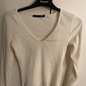 Vit ribbad långärmad tröja 157 XS - Säljer en vit ribbad långärmad tröja från 157 i storlek XS. Tröjan har v-ringning och är i ett mjukt, stretchigt material som sitter snyggt på kroppen. Perfekt att styla med jeans eller kjol för en clean look.