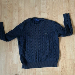 Mörkblå kabelstickad tröja från Gant - Säljer en klassisk mörkblå kabelstickad tröja från Gant med rund halsringning och broderad logga på bröstet. Säljer då den inte passar mig längre. Storleken är 164 (13-14 år) så sitter som xs.      Skick: 9/10. 