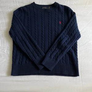 Mörkblå stickad tröja Polo Ralph Lauren - Storlek xl i barnstorlek ungefär m i herr storlek. Liten skada på höger armen syns inte vid användning. Kabel stickad ull tröja perfekt för kalla dagar.
