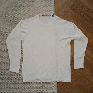 Vit stickad tröja från Gant - Vit stickad tröja från Gant i storlek L. Tröjan har ett diskret Gant-broderi på bröstet och är tillverkad i ett mjukt, strukturerat material. Klassisk rund halsringning och långa ärmar. Perfekt för en clean och stilren look.
