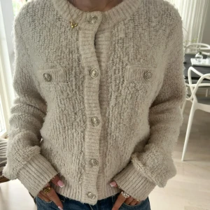 Beige stickad kofta med knappar - Supermysig beige stickad kofta med grov struktur och snygga silvriga knappar framtill. Koftan har långa ärmar, ribbade muddar och två dekorativa bröstfickor. Perfekt att slänga på sig när det är kyligt ute.🥰🥰