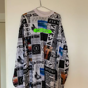 COLLUSION mönstrad långärmad tröja - Säljer en långärmad tröja från COLLUSION med collage-inspirerat tryck i svart, vitt och inslag av blått och grönt. Tröjan har rund hals och oversized passform, perfekt för dig som gillar streetstyle och unika prints.