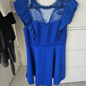 Blå spetsklänning från WalG - Supersnygg blå kortklänning från WalG med volangärmar och v-ringning. Överdelen har blommig spets och transparent mesh, medan kjolen är slät och lätt utsvängd. Perfekt för dig som vill sticka ut med en färgstark look! Använd 1 gång 550kr ny
