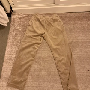 Beiga mjukisbyxor i sammet - Säljer ett par beiga mjukisbyxor i mjuk och glansig sammetskänsla. Byxorna har resår i midjan och raka ben med avslappnad passform. Perfekta för chill dagar hemma eller när du vill vara extra bekväm.
