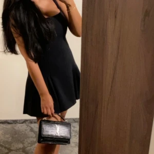 Svart kort klänning med smala axelband - Supersnygg svart kort klänning med smala axelband och lätt utsvängd kjol. Enkel och stilren design som ger en feminin siluett. Perfekt för dig som gillar en klassisk look med modern twist.