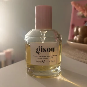 Gisou Honey Infused Hair Perfume - Gisou Honey Infused Hair Perfume i en rund glasflaska med ljusrosa lock. Parfymen är gyllengul och flaskan rymmer 50 ml. Doften är söt och lyxig med inslag av honung, perfekt för att fräscha upp håret med en mjuk och fräsch känsla.
