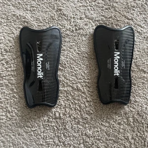 Monolit benskydd i kolfiber - Säljer ett par svarta benskydd från Monolit i kolfiber. De har en snygg, sportig form och är riktigt lätta men ändå stabila. Perfekta för dig som vill ha max skydd och smidig känsla på planen. Passar både träning och match.