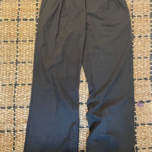 Grå kostymbyxor med raka ben - Snygga svarta kostymbyxor med raka ben och klassiska pressveck. Byxorna har hällor för bälte och två bakfickor med knappar. Relativt låg midja