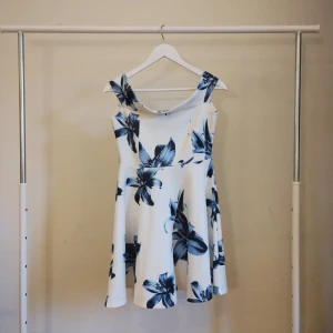 Vit blommig kortklänning Boohoo - Superfin vit kortklänning från Boohoo med stora blå blommor. Klänningen har breda axelband, lätt utställd kjol och en snygg, rund halsringning. Perfekt för dig som vill sticka ut med ett fräscht och somrigt mönster.