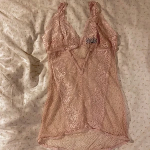 Rosa spetsig linnetopp från René Rofé - Supersöt ljusrosa linnetopp från René Rofé med spetsdetaljer och mesh. Djup v-ringning, tunna axelband och blommigt spetsmönster framtill. Perfekt för lager-på-lager eller som statement-piece. Materialet är mjukt och stretchigt.