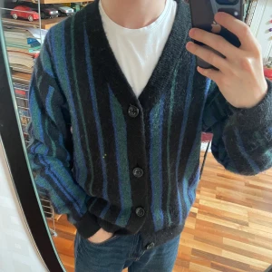 Randig kofta  - Säljer en skitsnygg och unik oversized, stickad kofta från Vailent med svarta, blå och gröna ränder. Koftan har v-ringning, stora svarta knappar och långa ärmar. Tröjan är tjock och varm, och är i storlek XS, men passar mer som S. Nästan helt oanvänd. 