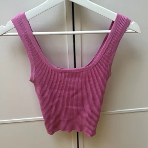 Ribbad rosa linnetopp - Säljer en ribbad rosa linnetopp med breda axelband och croppad passform. Toppen har en snygg, vågig nederkant och är perfekt för varma dagar. Enkel och stilren design som är lätt att matcha med jeans eller kjol.