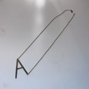Guldfärgat halsband med bokstav A - Snyggt halsband i guldfärg med en stor bokstav A som hänge. Kedjan är tunn och stilren med klassiskt lås. Perfekt accessoar för dig som vill ha något personligt och enkelt men ändå trendigt.