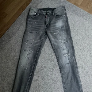 Grå jeans från Dsquared2 - Säljer ett par grå jeans från Dsquared2 med slitna detaljer och snyggt tvättad look. Byxorna har fem fickor, smal passform och klassisk knappgylf. Perfekta för dig som gillar streetstyle och vill sticka ut lite extra.