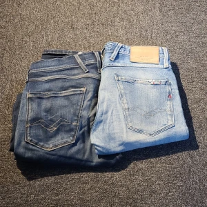 2 par Replay jeans, blå & ljusblå - Två par snygga Replay jeans i olika blå tvättar. Ena paret är mörkblå med klassiska bakfickor och den andra är ljusblå med slitningar. Båda har raka ben, femficksmodell och tydliga Replay-detaljer. Perfekta för dig som gillar en avslappnad men stilren look.
