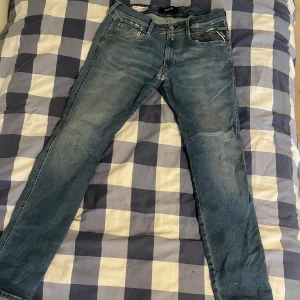 Blå Replay Hyperflex jeans, Anbass - Säljer ett par blå Replay Hyperflex Anbass jeans med klassisk femficksdesign och snygga slitningar. Jeansen har normal passform, raka ben och är tillverkade i stretchigt denim för extra komfort. Perfekta för dig som gillar en stilren och modern look.