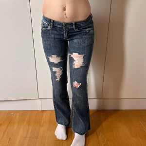Lågmidjade bootcut jeans vintage med hål y2k 2000s - Vintage jeans med hål både fram och bak. Superfint skick. Storlek 26. Innerbenslängd:73 midjemått: 36 stretch till 39. köp sker via köp nu, jag postar inom 24. Kvar tills markerad såld 