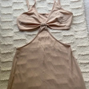 Ny. Beige ribbad midiklänning med cut out - Trendig beige ribbad klänning med smala axelband och snygg cut out-detalj framtill. Klänningen har en knut under bysten och är figurnära med en längre passform. Perfekt för dig som gillar minimalistisk och stilren look. Stretch.