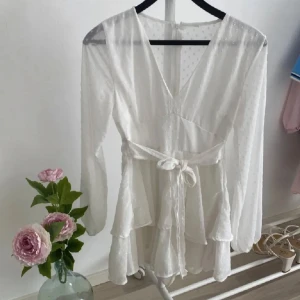 Vit omlottklänning med volanger - Säljer en elegant vit omlottklänning med v-ringning och knytband i midjan. Klänningen har även "shorts" under vilket är sååå praktiskt!💓 Är köpt för 600 och använda endast en gång! » priset kan diskuteras!💓