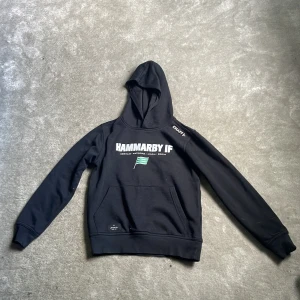 Svart Hammarby IF hoodie från Craft - Svart Hammarby hoodie storlek 146/152  från Craft med Hammarby IF-tryck på bröstet och grönvit flagga. Klassisk känguruficka framtill, huva och långa ärmar. Perfekt för dig som vill representera Hammarby på stan eller på match.