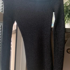Svart one shoulder glittrig tröja   - Säljer en svart, ribbad stickad tröja som är one shoulder  från MIS Knitewear i storlek XS. Tröjan har lång ärm och en tight passform som sitter snyggt på kroppen. 