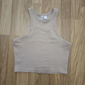 Beige ribbad croppad linnetopp - Säljer en beige croppad linnetopp från h&m Divided. Toppen är ribbad och har en sportig, ärmlös design med breda axelband och rund halsringning. Perfekt för varma dagar eller att styla lager på lager.