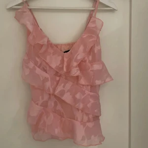Rosa volangig linnetopp - Supersöt rosa linnetopp med flera lager volanger och tunna axelband. Toppens tyg är lätt och halvtransparent med ett subtilt blommigt mönster. Perfekt för en somrig look när du vill sticka ut lite extra.💗💗💗