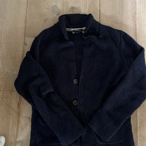 Mörkblå stickad kavaj från esprit - Säljer en mörkblå stickad kavaj från Only & Sons. Jackan har en avslappnad passform, knäppning framtill och två fickor. Perfekt för dig som vill ha en stilren men bekväm look. Märkt med 'Handcrafted' på insidan. Den är i lite stretchigt material och i storlek S. Skriv gärna om ni har några funderingar!!