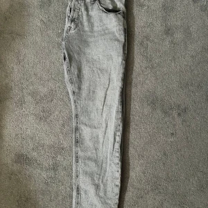 Grå jeans från Jack & Jones - Säljer ett par grå jeans från Jack & Jones med klassisk femficksdesign och dragkedja. Jeansen har en rak passform och är tillverkade i denim. Perfekta för en avslappnad stil.