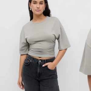 Grå croppad topp med rynkdetalj - Säljer en stilren grå croppad topp med rynkdetalj i midjan från Ginatricot. Toppen har korta ärmar och rund halsringning, perfekt att matcha med jeans eller kjol. Använts 1 gång då den är för liten
