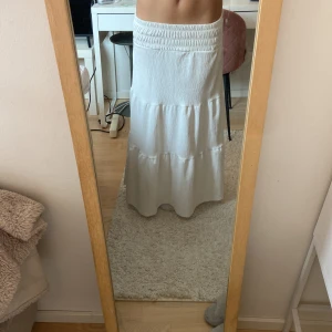Vit långkjol med volang - Säljer en vit långkjol med bred resår i midjan och volangdetaljer. Kjolen är från Gina tricot och är köpt förra sommaren och använt en del. Säljer då den är för kort (jag är 158)