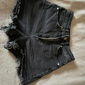 Svarta jeansshorts med fransar - Säljer ett par svarta jeansshorts med hög midja. Shortsen har dragkedja och knapp framtill samt klassiska fickor. Perfekta för sommaren!