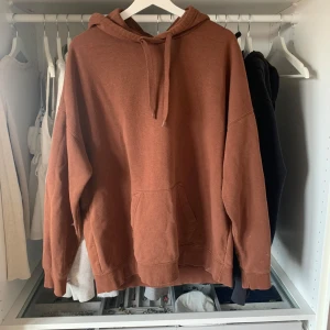 Brun hoodie med ficka - Säljer en brun hoodie med huva och dragsko. Tröjan har en stor magficka och är tillverkad i mjukt bomullsmaterial. Perfekt för en avslappnad stil och passar bra till jeans eller mjukisbyxor. har en defekt, kolla bild. 