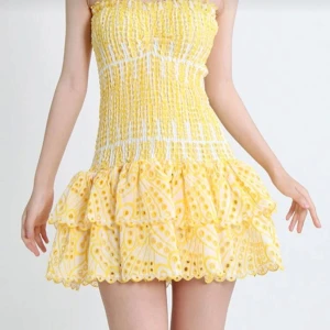 Gul volangklänning  - Supersöt gul kortklänning med smockad överdel och volangkjol. Klänningen är ärmlös och har ett broderat mönster i gult och vitt. Perfekt för sommarens alla tillfällen!