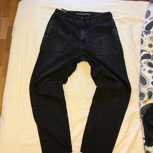 Svarta byxor från Stone Island - Säljer ett par svarta byxor från Stone Island med klassisk logotyp-patch på bakfickan. Byxorna har normal passform och raka ben. Väldigt stibilt skick förutom märke från telefon vid fickan. Annars inget hål eller så. Midja 32. Skickar direkt vid köp. Skriv vid frågor!