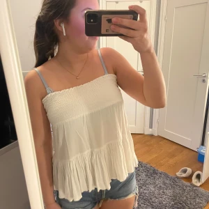 Vit kjol från 157 - Säljer en söt vit kjol från 157 med smockdetaljer i midjan och volanger. Perfekt för varma dagar och ger en luftig känsla. Kjolen har en kort längd och är lätt att matcha med olika toppar.