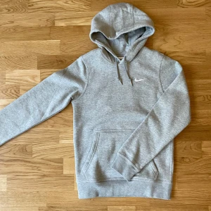 Grå hoodie från Nike - Säljer en klassisk grå hoodie från Nike med vit logga på bröstet. Tröjan har huva med dragsko och en stor magficka. Perfekt för en avslappnad stil och enkel att matcha med det mesta.       Nypris: 799 mitt pris: 599 då den är helt ny och aldrig använd då den är för liten på mig!
