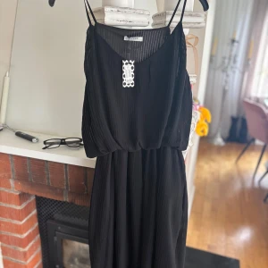 Svart plisserad långklänning från Pieces - Säljer en svart plisserad långklänning från Pieces med smala axelband och avslappnad passform. Perfekt för dig som vill ha en stilren och enkel look. Klänningen har en lätt och luftig känsla.