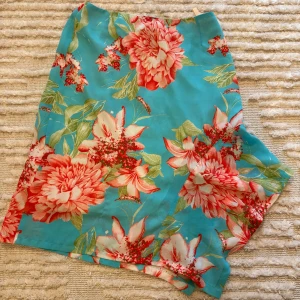 Turkos blommig kjol från Maria Westerlind - Säljer en färgglad turkos kjol från Maria Westerlind med stora blommor i rött, rosa och vitt. Kjolen har en lätt A-linjeform och är perfekt för varmare dagar. Tunt och mjukt tyg som känns luftigt.