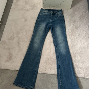 Blå bootcut jeans med broderade bakfickor - Säljer ett par blå bootcut jeans med snygga broderade detaljer och knappar på bakfickorna. Jeansen har klassisk femficksdesign och lätt slitna partier framtill för en cool look.