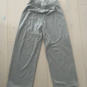 Grå mjukisbyxor från Pull&Bear - Gråa mjukisbyxor från Pull&Bear med bred resår i midjan och raka, vida ben. Byxorna är tillverkade i mjukt bomullsmaterial och har en enkel, stilren design utan synliga detaljer eller fickor. 