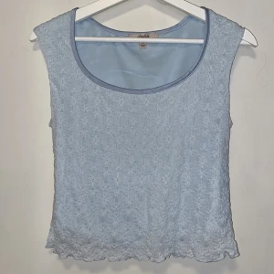 Ljusblå spetstopp från Atelier - Säljer en oanvänd ljusblå topp från Atelier. Toppen har ett spetsmaterial med blommönster och rund halsringning. Köpt i New York men har aldrig kommit till användning.