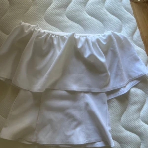 Vit offshoulder volangtopp - Säljer en vit offshoulder topp med volangdetalj. Toppen har en luftig och somrig känsla, perfekt för varma dagar. Den är axelbandslös och har en bred volang som täcker överdelen.