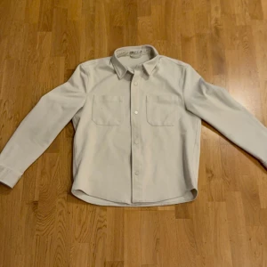 Overshirt  från Zara - Säljer en stilren vit skjorta från Zara med klassisk krage och två bröstfickor. Skjortan har långa ärmar och knäppning framtill. Perfekt för dig som gillar en enkel och clean look.