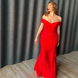 Röd bal/fest klänning med slits och offshoulder - Säljer en elegant röd långklänning med offshoulder och djup v-ringning. Klänningen har draperade detaljer längs midjan och en hög slits på ena sidan. Perfekt för bal eller fest. Snygg och figurnära passform. Den är använd en gång och kem tvättad efter. Inget slitage och som ny. Nypris ligger på 3000kr